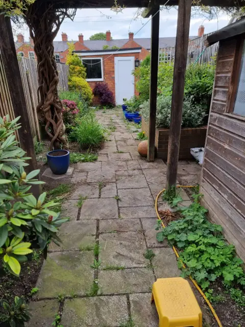 Weed-covered paving slabs running down a terraced rear garden before the work