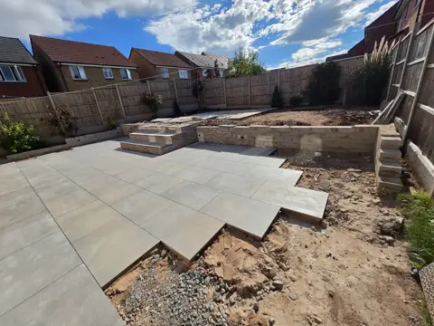 Rear garden mid-build with new porcelain patio, bare soil and an unfinished retaining wall