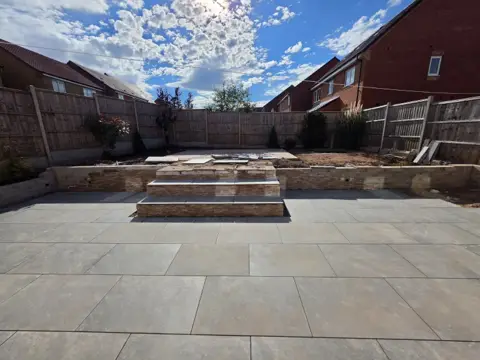 Unfinished brick steps and retaining wall behind a new porcelain patio