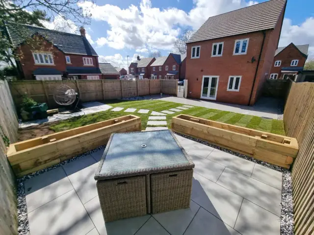 Landscaped garden with raised sleeper beds, lawn and porcelain patio by The Green Team