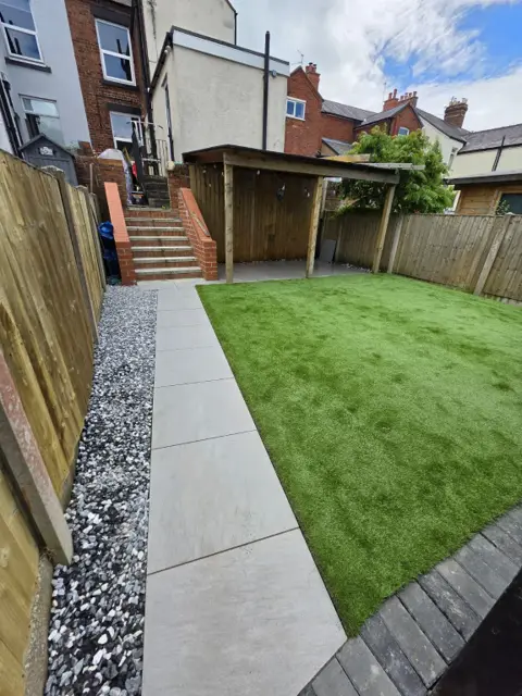 The same rear garden finished with artificial grass, a porcelain path and decorative stone